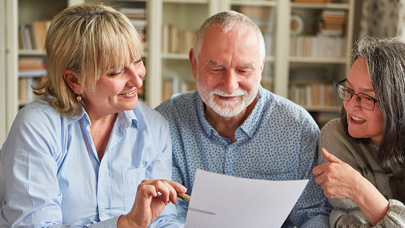 A senior couple reviewing paperwork with a volunteer, symbolizing the process of requesting a walking companion.