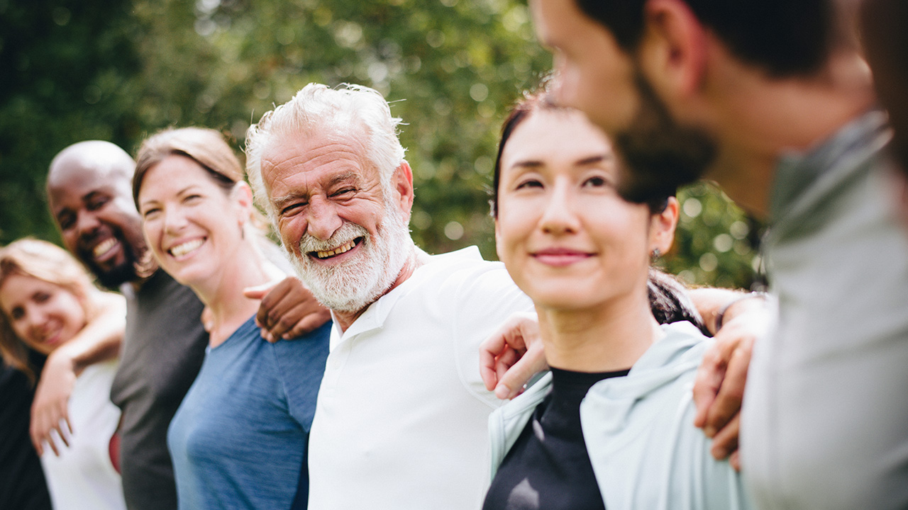 A diverse group of seniors and volunteers smiling together outdoors, symbolizing community, connection, and well-being.